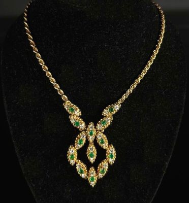 a gold necklace with emerald and white stones on a black mannequin