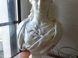 une statue représentant une femme assise sur une table près d'une fenêtre