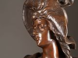 a bronze statue of a woman with a hat on her head