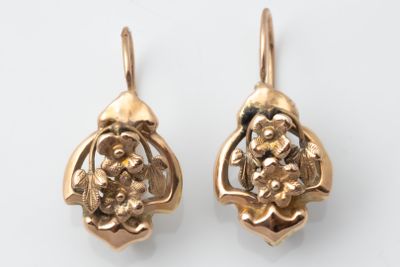 pair of gold earrings with flowers and leaves on them on a white surface