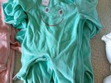 three baby clothes laid out on the floor next to a stuffed animal