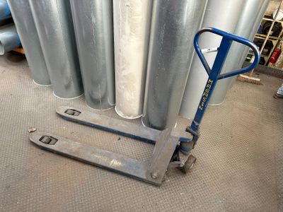 un diable bleu posé devant une pile de tuyaux métalliques