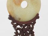 Beignet en jade sculpté de style chinois posé sur un socle, sur fond blanc