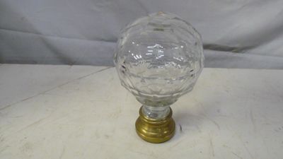 une photo montrant un verre et un bouton en laiton posés sur une table blanche