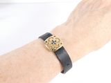 someone is wearing a black leather bracelet with a gold square design