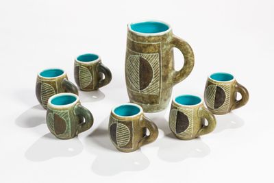 five cups and a jug sitting on a white surface