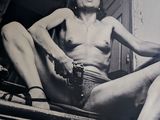 photographie en noir et blanc d'une femme nue assise sur des marches, un pistolet à la main