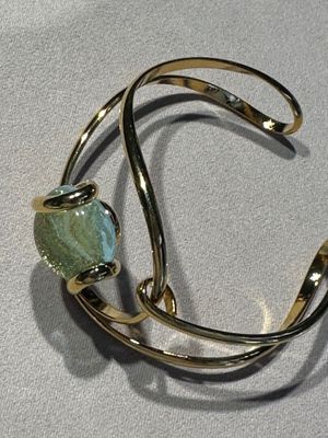bracelet manchette plaqué or, orné d'une pierre verte sur un fond blanc