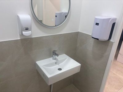 une salle de bains équipée d'un lavabo, d'un miroir et d'un distributeur de savon fixé au mur