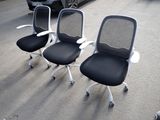 three office chairs sitting in a parking lot with a car in the background