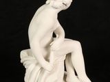 white statue of a woman sitting on a rock with her legs crossed