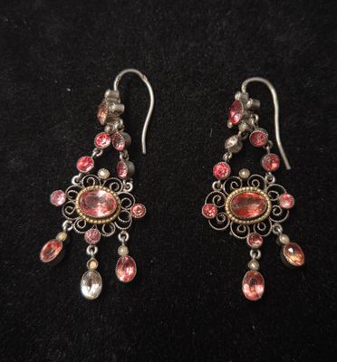 une paire de boucles d'oreilles roses et argentées posées sur un fond noir