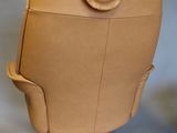 beige leather chair with wooden legs and a leather bag on the back of it