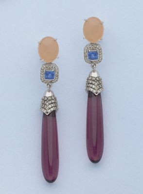 une paire de boucles d'oreilles ornées de pierres roses et bleues sur un fond blanc