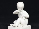 une petite statue blanche représentant un garçon assis sur un bloc
