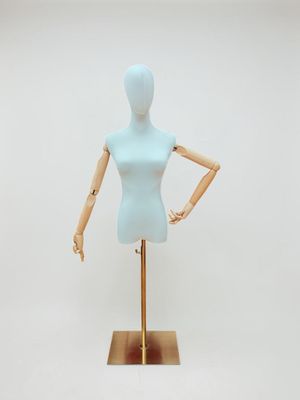 un mannequin féminin posé sur un socle doré, devant un fond blanc