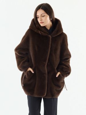 La femme porte un manteau de fourrure marron et un pantalon noir.