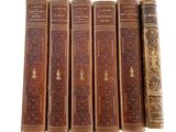 six old books are lined up in a row on a white surface