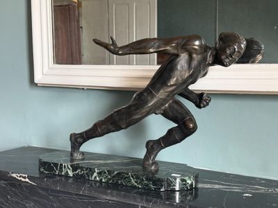 une statue en bronze représentant un homme en train de courir, posée sur un socle en marbre