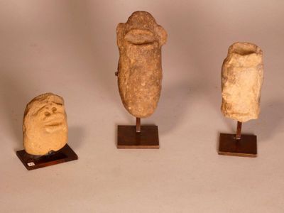 three stone heads on wooden stands on a white surface