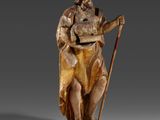 une statue en bois représentant un homme tenant une canne et un sac