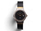une image représentant une montre-bracelet noire et dorée posée sur une surface blanche