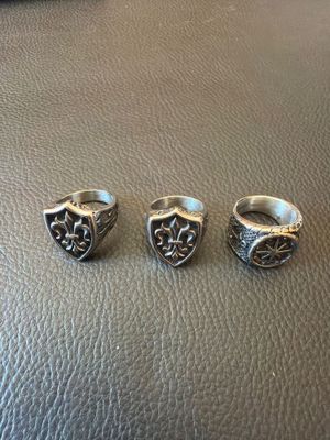 trois anneaux en argent sur une surface en cuir, l'un orné d'un bouclier et l'autre d'une fleur