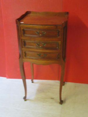 a small wooden table with drawers on it in front of a red wall