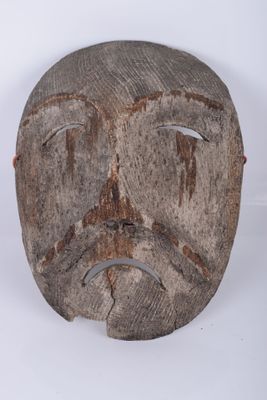 un vieux masque en bois posé sur une surface blanche, avec un fond blanc