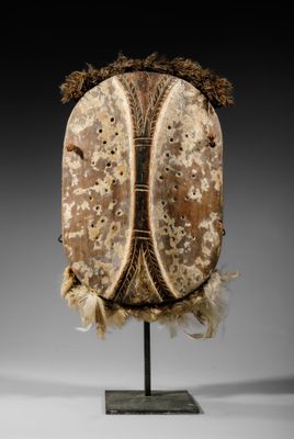 un grand masque en bois orné de plumes, posé sur un socle