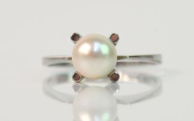 un gros plan d'une bague en perle blanche posée sur une surface blanche