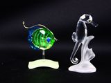 two glass fish figurines on a black surface with a black background