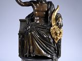 une statue antique en bronze représentant un homme assis sur une chaise