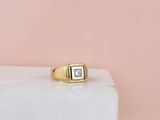 Une bague en or sertie d'un diamant taille princesse repose sur un bloc de marbre blanc