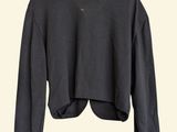 a black cropped sweater hanging on a hanger on a white wall