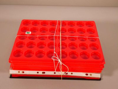 une pile de barquettes en plastique rouges percées de trous