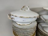 a stack of white and gold china dishes on a shelf