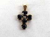 un pendentif en forme de croix en or, orné de pierres noires sur fond blanc