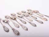 six cuillères en argent sont alignées sur une surface blanche
