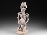 une statue représentant un squelette tenant un bol posé sur une table