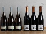 six bottles of wine are lined up on a wooden table