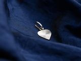 a close up of a silver heart charm on a blue fabric