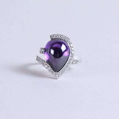 a close up of a purple heart shaped ring with diamonds on a white surface