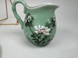 a green pitcher with flowers on it sitting on a table