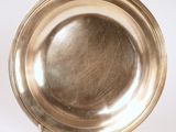 assiette en argent posée sur un support, sur une surface blanche, avec un fond blanc