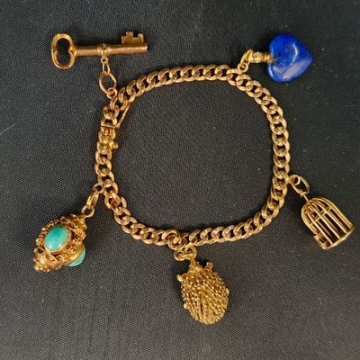 un gros plan sur un bracelet en or orné de breloques et d'une cage à oiseaux