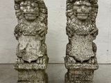 pair of stone lion heads on pedestals in front of a white wall