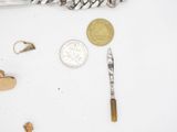 a silver chain, a silver knife, a coin, and a pair of scissors on a white surface