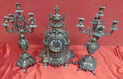 five silver candlesticks and a clock sitting on a red cloth