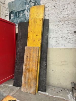 Plusieurs morceaux de bois sont posés par terre devant une porte rouge